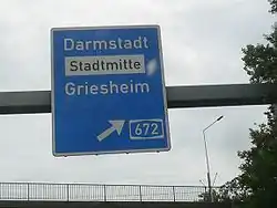 A sign on a German Autobahn: destination=Darmstadt;Stadtmitte;Griesheim destination:colour=;white;[2] destination:ref=A 672