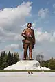 1/4 Statue of Kim Il-sung (tourism=artwork and artwork_type=statue) on its white base with trees in the background seen from the ground.