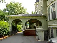 A roof which is built above the entrance. To the left, there is a passage to allow cars to pass through, in the middle is the covered entrance to the door location, to the right is the house.